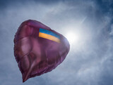 Fototapeta  - An inflatable pink balloon in the shape of a heart with a painted Ukrainian flag on the background of the sky and the bright sun..Copy stace