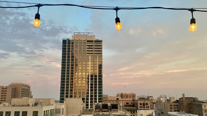 Wall Mural - LOS ANGELES, CA, JUN 2021: new multi-storey apartment building in Downtown with sunset clouds and light reflecting on the windows. String of light bulbs in foreground, top of image