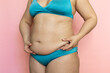 © Юля Бурмистрова - Pinch woman sagging belly with fingers closeup, folds on stomach, loose skin and cellulite. Naked overweight plus size girl on pink background in blue underwear. Concept of dieting and body control.