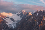 Fototapeta Do pokoju - Scenic aerial view to high snow mountains in early morning at dawn. Awesome scenery with sunlit gold pinnacle in cloudy sky at sunrise. Morning landscape with snow mountain peak in golden sunlight.