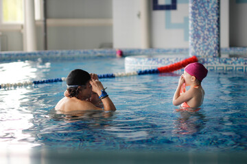 Happy kid toddler learns to swim with coach in pool, daddy grandpa teaches kids to swim and dive in pink swimming cap