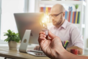 Wall Mural - Human hand holds light bulb on workplace background. Save energy concept.