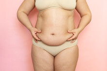 Measure Woman Sagging Belly Closeup, Folds On Stomach, Loose Skin And Cellulite, Obesity. Naked Overweight Plus Size Girl On Pink Background In Beige Underwear. Concept Of Dieting And Body Control.