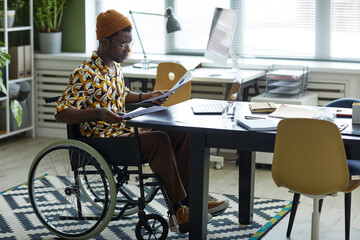 Full length portrait of black young man in wheelchair wearing creative fashion while working in office, copy space