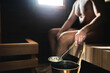 © terovesalainen - Man in sauna. Finnish steam room bath. Person pouring water on the hot stones from bucket. Traditional relaxation and wellness in Finland. Dark wooden health spa home or in hotel.