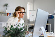 © Andrii  - Pretty mature business woman in glasses works at a computer in the office. Secretary or accountant working online