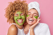 © wayhome.studio - Positive women feel joyful smile broadly keep eyes closed apply green nourishing mask and patches dressed in white t shirts undergo beauty procedures isolated over pink background. Facial treatment
