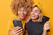 © WHstudio Leushin N - Two happy surprised women enter information from banking credit card confirm purchase enjoy online shopping in mobile application have glad expressions pose indoor against yellow studio wall