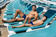 © Andrii - A young athletic man and his son are smiling happily and sunbathing on a sun lounger on a sunny day at the hotel. Happy family vacation at a hotel in the resort. Summer holidays and tourism.
