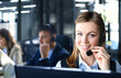 © ty - Female customer support operator with headset and smiling, with collegues at background.