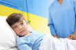 Humanitarian aid and medical care for war in Ukraine. Child with post traumatic stress in hospital bed. Boy looking at camera. Yellow and blue colors of the flag of Ukraine. Ukrainian refugees injured