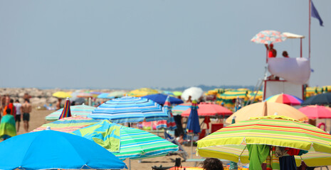 Wall Mural - colorful umbrellas on the crowded beach on the sea coast in summer and the lifeguard watchtower