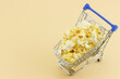 Shopping trolley fully filled with popcorn isolated on beige background with copy space. Unhealthy food concept. Top view