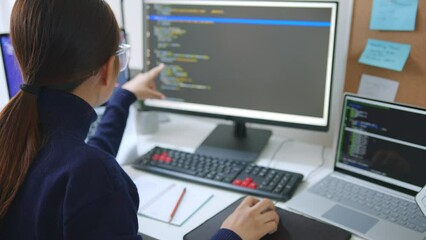 Young Asian woman, developer programmer, software engineer, IT support, wearing glasses working on computer to check coding in bugging system. Back view
