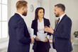 © Studio Romantic - Group of people in suits having a conversation. Three serious business professionals discussing something. Defendant, defense lawyer and relative standing in courtroom, holding documents and talking