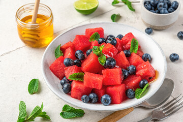 Wall Mural - Summer salad with watermelon, blueberry, honey, lime juice and mint in a plate with cutlery. close up