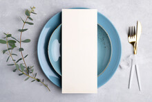 Vertical Menu Card Mockup With Festive Wedding Or Birthday Table Setting With Golden Cutlery, Eucalyptus, Blue Ceramic Plate On Grey Background. Restaurant Menu Concept. Flat Lay, Top View