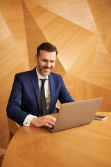 Successful businessman working on laptop sitting by desk at modern office