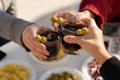 Three people clinking with vermouth glasses in a sunny day. Just three arms cropped doing a toast. Friends enjoying drinks and food.