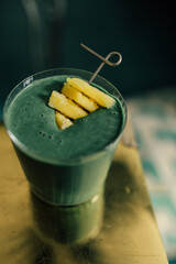 Wall Mural - green spirulina smoothie with pineapple on brass, gold table and teal background	