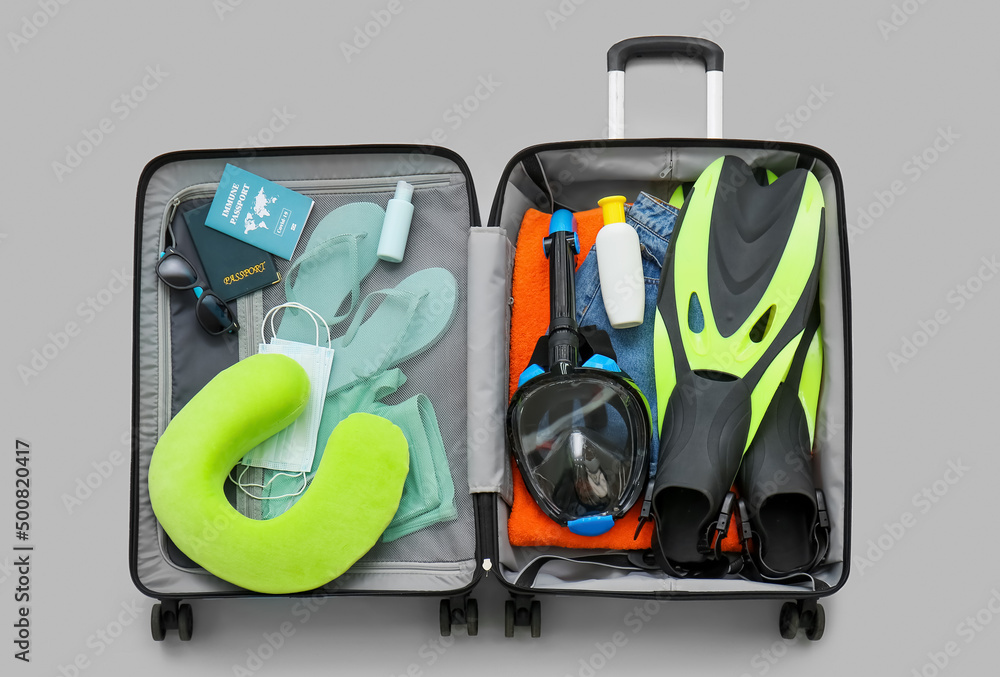 Suitcase with beach accessories, snorkeling mask and immune passport on light background