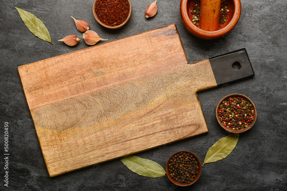New cutting board with spices on dark background