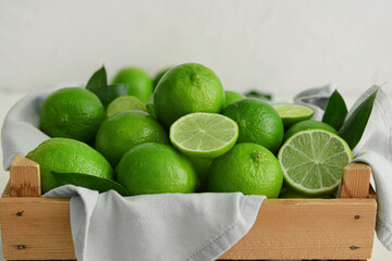 Wooden box with fresh ripe limes on light background, closeup