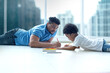 © chomplearn_2001 - Happy African family, lying on the floor at home, father helping little cute curly son drawing picture, out of window high building view in blur background