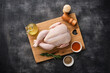 A whole raw chicken resting on a wooden board against a dark background. Preparing raw chicken. Top view