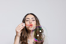 Young Woman Blowing Soap Bubbles Against Gray Background