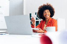 Happy Businesswoman Holding Windmill Model Sitting With Laptop At Desk