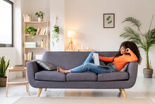Young Woman With Laptop Sitting On Sofa In Living Room At Home