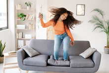 Smiling Woman With Tousled Hair Dancing On Sofa At Home