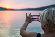 Senior Woman Photographing Sunset Through Smart Phone On Vacations