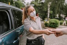 Young Woman Wearing Protective Face Mask Giving Car Key To Friend At Parking Lot