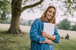 © Westend61 - Smiling beautiful woman with laptop standing in park