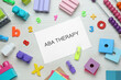 Flat lay composition with phrase ABA Therapy and colorful toys on white wooden table