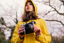 Young Woman Wearing Yellow Raincoat Standing With Camera In Forest