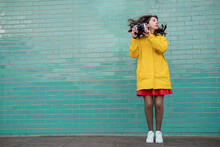 Woman With Tousled Hair Jumping With Camera In Front Of Wall