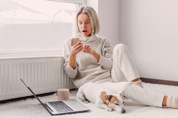 Wall Mural - Happy middle aged woman with dog using her laptop at cozy white home