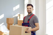 © Studio Romantic - Portrait of young worker from modern professional moving company or express delivery service. Happy handsome man in workwear uniform standing inside house, holding cardboard box and smiling