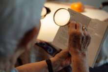 Senior Woman With Magnifying Glass Reading Book At Home