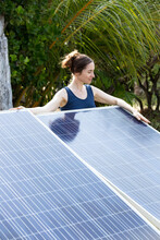 Woman Standing Behind Solar Panels Under Palm Trees
