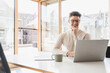 © Westend61 - Smiling young businessman using laptop at desk in office
