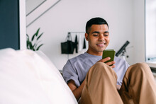 Smiling Man Surfing Net Through Smart Phone At Home