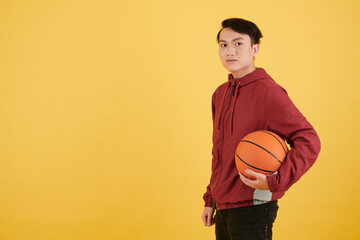 Wall Mural - Studio portrait of young Asian man holding basketball ball