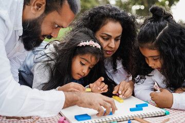 Wall Mural - happy indian family having fun painting with children outdoor at city park - focus on little girl fa