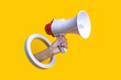 Female hand holds a megaphone in a round hole on a yellow background.