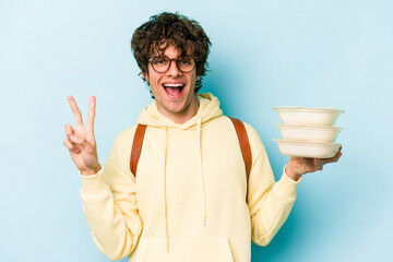 Young caucasian student man holding a tupperware isolated on blue background showing number two with fingers.