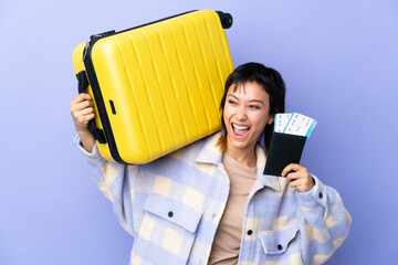 Wall Mural - Young Uruguayan woman over isolated purple background in vacation with suitcase and passport